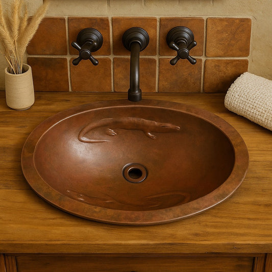 Custom oval copper sink with lizard reliefs installed in a rustic bathroom wth bronze faucet and wood countertop